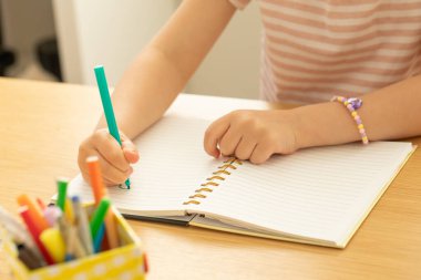 Şirin, düşünceli küçük kız masada oturan not defterine komik bir resim çiziyor. Küçük çocuk ressam evde dinlenen yaratıcılığını ifade ediyor. Mutlu çocukluk