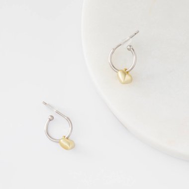 Minimalist gümüş ve altın küpeler mermer bir kürsüde ve beyaz arka planda kalp şeklinde. Küpe kataloğu. Şık kadın mücevherleri..