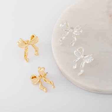 Mermer zemin ve beyaz zemin üzerinde fiyonk şeklinde altın ve gümüş küpeler. Mücevher kataloğu. Moda mücevherleri..