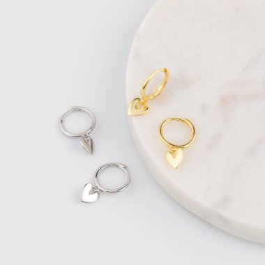 Bir çift altın ve beyaz arka planda kalp şeklinde gümüş küpeler. Modaya uygun mücevher konsepti. Mücevher kataloğu.