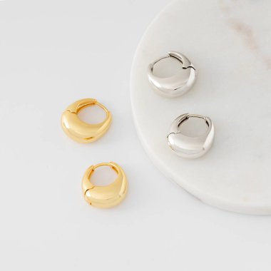 Şık altın ve gümüş halka küpeler beyaz arka planda lüks mermer bir kürsüde zarif bir şekilde yerleştirilmiştir. Mücevher kataloğu.