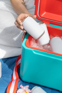 Elinde içecek kutusu olan bir kadın termos kutusunun üzerinde buz küpleriyle birlikte yakın çekim yapıyor. Pikniğe geri dönüşümlü teneke kutuda soğuk içecek alan bir kadın. Boş ambalaj