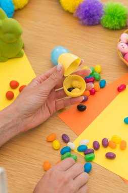 Paskalya kutlamaları için plastik paskalya yumurtalarını yumurta şeklinde şekerlerle dolduran bir kadın. Yumurta avı konsepti. Mutlu Paskalyalar