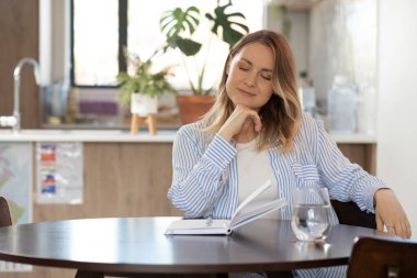 Su bardaklı ve açık organizatörlü bir kadın yuvarlak masada oturuyor. Hırslı kadın, stüdyo dairesindeki günlüğü doldurmak için gelecek için hedefler belirliyor.