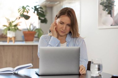 Kablosuz kulaklıklı kadın laptopta masada oturuyor. Kadın girişimci evde kalan hizmetleri ve ürünleri desteklemek için İnternet kullanıyor