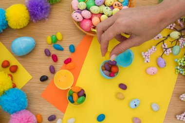 Paskalya kutlamaları için plastik paskalya yumurtalarını yumurta şeklinde şekerlerle dolduran bir kadın. Yumurta avı konsepti. Mutlu Paskalyalar