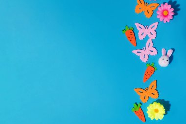 Bahar kutlamaları için mavi arka planda keçeli kelebekler, havuçlar ve çiçeklerle süslenmiş Paskalya süsleri. Boşluğu kopyala
