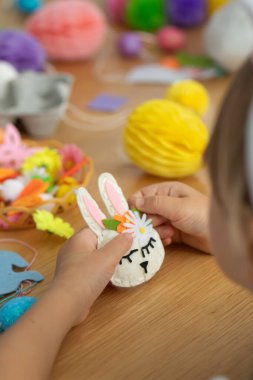 Çocuk eğlencesi ve bahar tatilleri için ev yapımı süslemeleri olan yaratıcı Paskalya el sanatları. Paskalya tavşanı keçeden yapılmış, kendi elleriyle bir kızın elinde. ÇEVİR