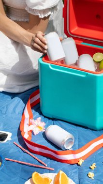 Elinde içecek kutusu olan bir kadın termos kutusunun üzerinde buz küpleriyle birlikte yakın çekim yapıyor. Pikniğe geri dönüşümlü teneke kutuda soğuk içecek alan bir kadın. Boş ambalaj