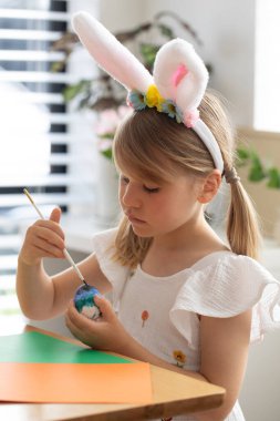 Tavşan kulaklı şirin bir kız. Masada otururken paskalya yumurtasını boyuyor. Paskalya için hazırlanılıyor.