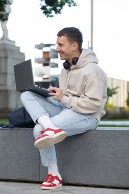 Genç serbest çalışan bir erkek halka açık bir parkta dizüstü bilgisayarla çalışıyor. Uzak çalışma konsepti