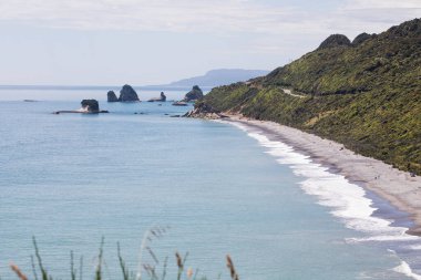 Kayalık çıkıntıları ve yeşil tepeleri olan manzaralı kıyı manzarası. Yeni Zelanda