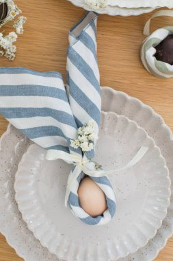 Paskalya yumurtası keten peçeteye sarılmış kulaklı tavşan şeklinde. Paskalya dekoru ve sofra kurma fikri. Mutlu Paskalyalar.