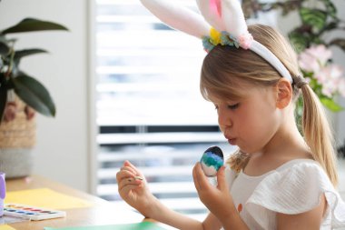 Çocuk güneşli odada yaratıcı Paskalya yumurtası resminin keyfini çıkarıyor. Mutlu Paskalyalar
