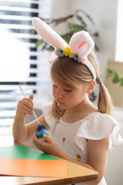 Tavşan kulaklı şirin kız Paskalya yumurtalarını boyayla süslüyor. Mutlu Paskalyalar.