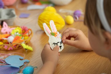 Çocuk eğlencesi ve bahar tatilleri için ev yapımı süslemeleri olan yaratıcı Paskalya el sanatları. Paskalya tavşanı keçeden yapılmış, kendi elleriyle bir kızın elinde. ÇEVİR