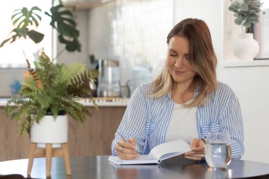 Evde rahat bir atmosferi olan deftere yazı yazan bir kadın. Neşeli kadın modern stüdyo dairede fikirler ve planlar yaratıyor.