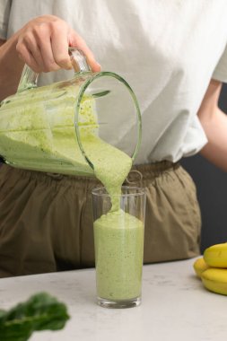 Mutfakta blenderdan cama yeşil smoothie döken bir kadın. Detoks konsepti, vejetaryen yemekleri.