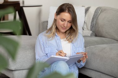 Mutlu kadın yere oturmuş günlüğe ilginç şeyler yazıyor. Neşeli kadın oturma odasında verimli bir yıl için planlar yapar. Geleceği hayal etmek