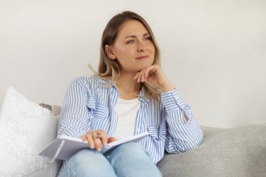 Not defterli sarışın bir kadın rahat koltukta oturuyor. Kendini işine adamış bir kadın geleceği düşünür oturma odasında iddialı planlar yapar. Zaman yönetimi