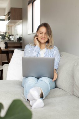 Konforlu oturma odasında dizüstü bilgisayar kullanan bir kadınla rahat bir ofis kurmak. Merkez Ofis