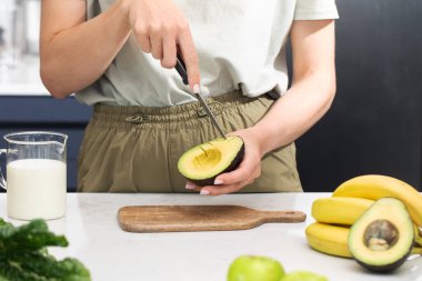 Bir kadın olgun bir avokadoyu keser. Taze meyve ve avokado dilimleri ile sağlıklı kahvaltı hazırlığı. Diyet
