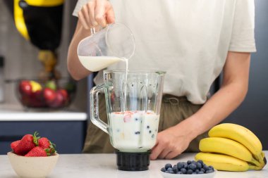  Kadın blender 'a meyve ve blender dolduruyor. Ev mutfağında blender ve sütle taze meyve püresi.
