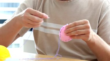 Paskalya oyuncağını pembe yumurta şeklinde dikmek için iğne ve iplik kullanan bir adam. DIY. Sanat ve zanaat kavramı. Mutlu Paskalyalar