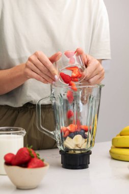 Bir kadın miksere taze çilek ekler. Sağlıklı bir yaşam için çilekli ve muzlu taze meyve püresi.