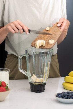  Kadın, muz parçalarını miksere koyuyor. Kahvaltıda taze meyve ve blender ile sağlıklı muz suyu hazırlıyorum.