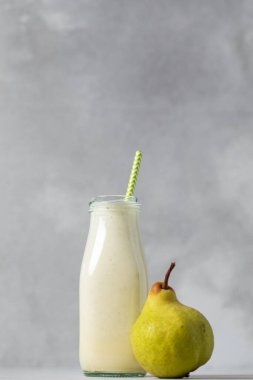 Cam şişede taze armut püresi ve gri arka planda saman. Detoks ve diyet kavramı