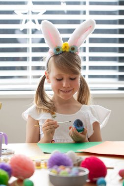 Paskalya yumurtası boyayan küçük mutlu kız tavşan kulaklığı takıyor. Mutlu Paskalyalar. Paskalya işçiliği