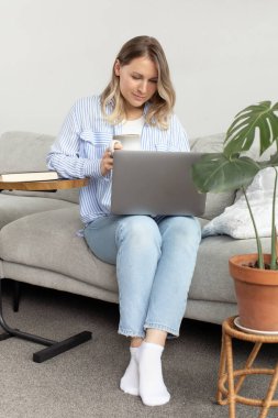 Evde rahat bir ortamda kahve ve dizüstü bilgisayarla dinlenen bir kadın. Laptop kullanılıyor