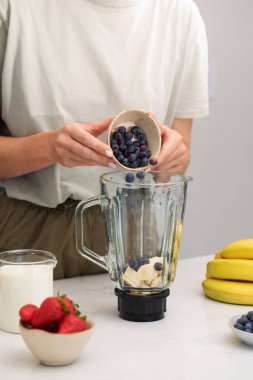 Bir kadın miksere taze yaban mersini ekler. Sağlıklı bir yaşam için çilekli ve muzlu taze meyve püresi.