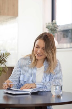 Evde rahat bir atmosferi olan deftere yazı yazan bir kadın. Neşeli kadın modern stüdyo dairede fikirler ve planlar yaratıyor.