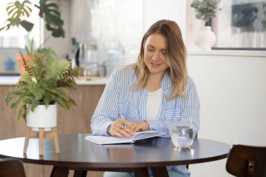 Evde rahat bir atmosferi olan deftere yazı yazan bir kadın. Neşeli kadın modern stüdyo dairede fikirler ve planlar yaratıyor.