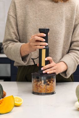 Sağlıklı yemek hazırlamak için mutfakta el blenderi kullanan bir kadın. Vejetaryen yemeği kavramı