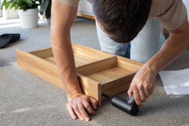 Kablosuz matkapla mobilya montajı yapan bir adam. Modern bir oturma odasında kablosuz matkapla ev eşyaları montajı. Talimatlar