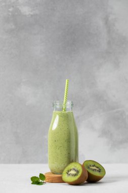 Gri arka planda saman bulunan cam şişede taze kivi smoothie. Detoks kavramı