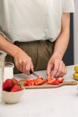 Çilek kesen kadın. Modern bir mutfakta sağlıklı bir kahvaltı için taze meyve ve meyve hazırlıyorum.