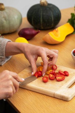 Dişi eller, kiraz domateslerini tahta kesme tahtasıyla sebze dilimliyor. Vejetaryen yemekleri kavramı