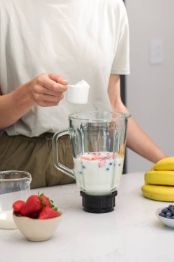 Kadın meyve suyuna bir kepçe protein tozu ekliyor. Sağlıklı bir kahvaltı için blenderlı taze meyve püresi yapıyorum. Diyet ve detoks kavramı