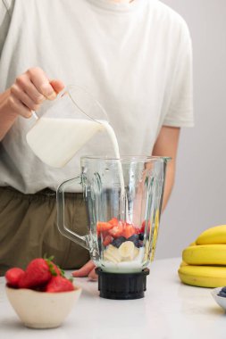  Kadın blender 'a meyve ve blender dolduruyor. Ev mutfağında blender ve sütle taze meyve püresi.