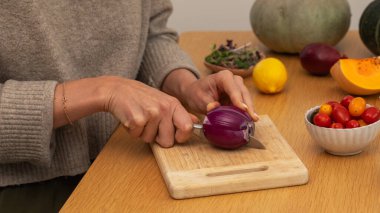 Ahşap kesme tahtasının üzerinde taze malzemelerle kırmızı soğan doğrayan kadın elleri. Vejetaryen yemekleri kavramı