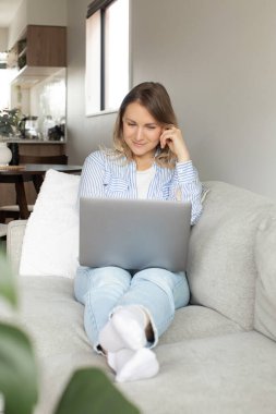 Odaklanmış kadın oturma odasındaki rahat koltukta oturup dizüstü bilgisayardan video izliyor. Sarışın kadın defter bilgisayarından çevrimiçi ders dinliyor. Merkez Ofis