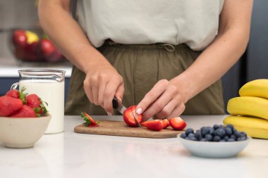 Çilek kesen kadın. Modern bir mutfakta sağlıklı bir kahvaltı için taze meyve ve meyve hazırlıyorum.