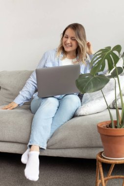 Genç bir kadın oturma odasındaki yumuşak kanepede dizüstü bilgisayar tutarak gülüyor. Sarışın, serbest çalışan bir kadın. İnternette çalışmaktan mutlu. Ofis konforu