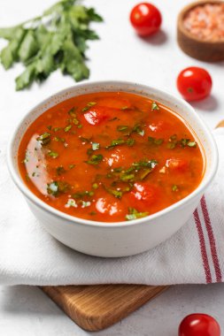 Domatesli taze sebze çorbası ve keten peçetedeki beyaz kasede otlar. Vejetaryen menüsü. 