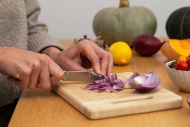 Ahşap kesme tahtasının üzerinde taze malzemelerle kırmızı soğan doğrayan kadın elleri. Vejetaryen yemekleri kavramı