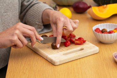 Dişi eller, kiraz domateslerini tahta kesme tahtasıyla sebze dilimliyor. Vejetaryen yemekleri kavramı